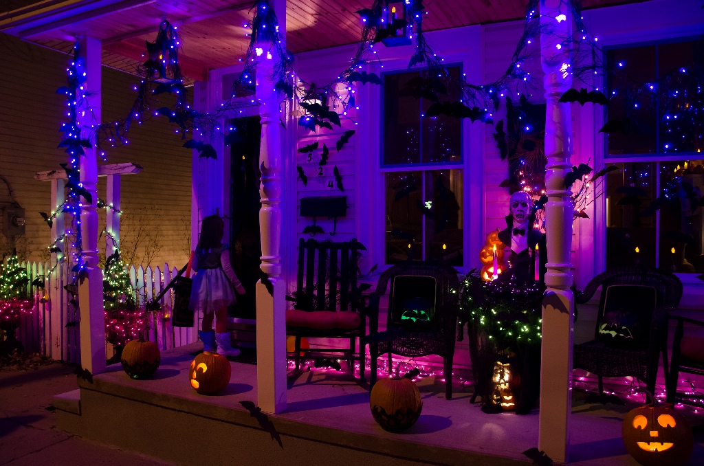 Halloweenske dekorácie na drevenej verande — svetelná reťaz, vyrezávané tekvice a papierové netopiere