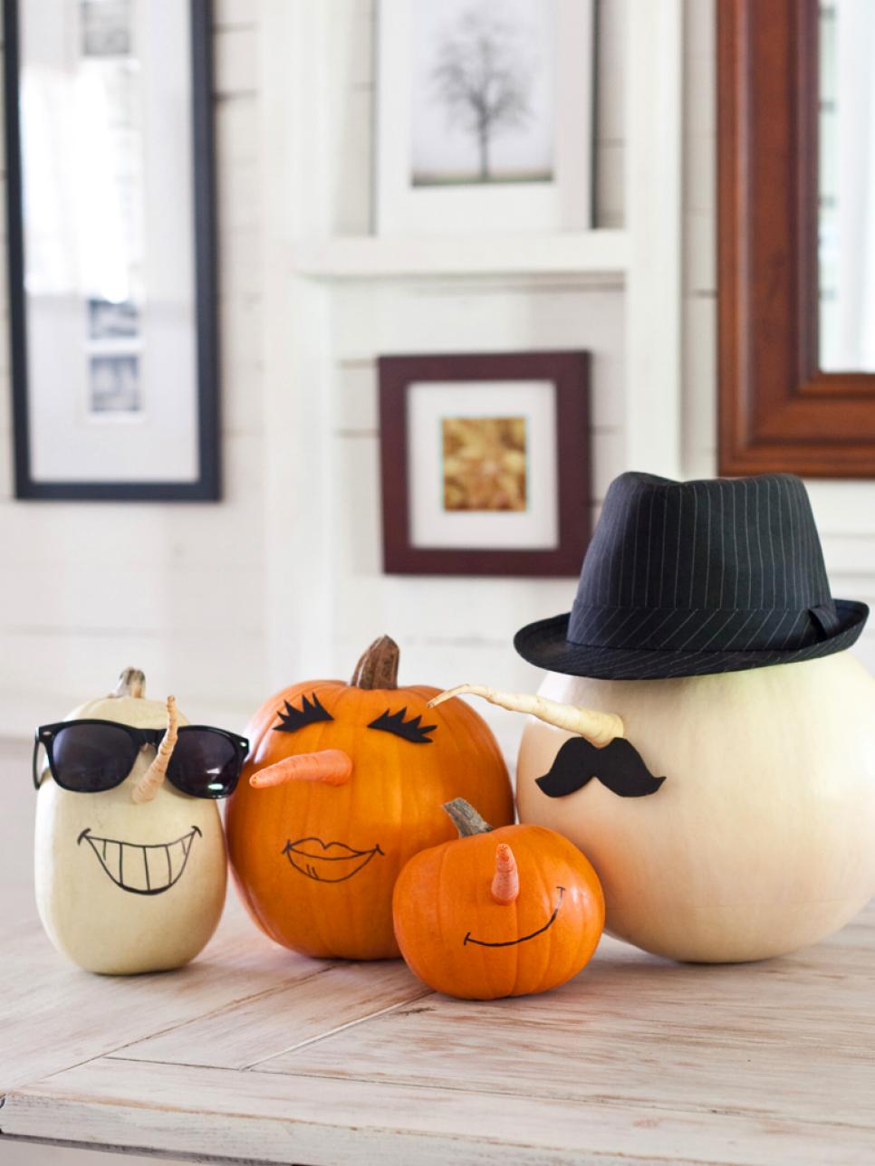 Halloweenska dekorácia z tekvíc s nakreslenými tvárami, klobúkom a okuliarmi ako tekvicová rodina