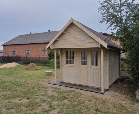 Drevený záhradný domček BUNKIE – čelný pohľad s tehlovou stodolou v pozadí