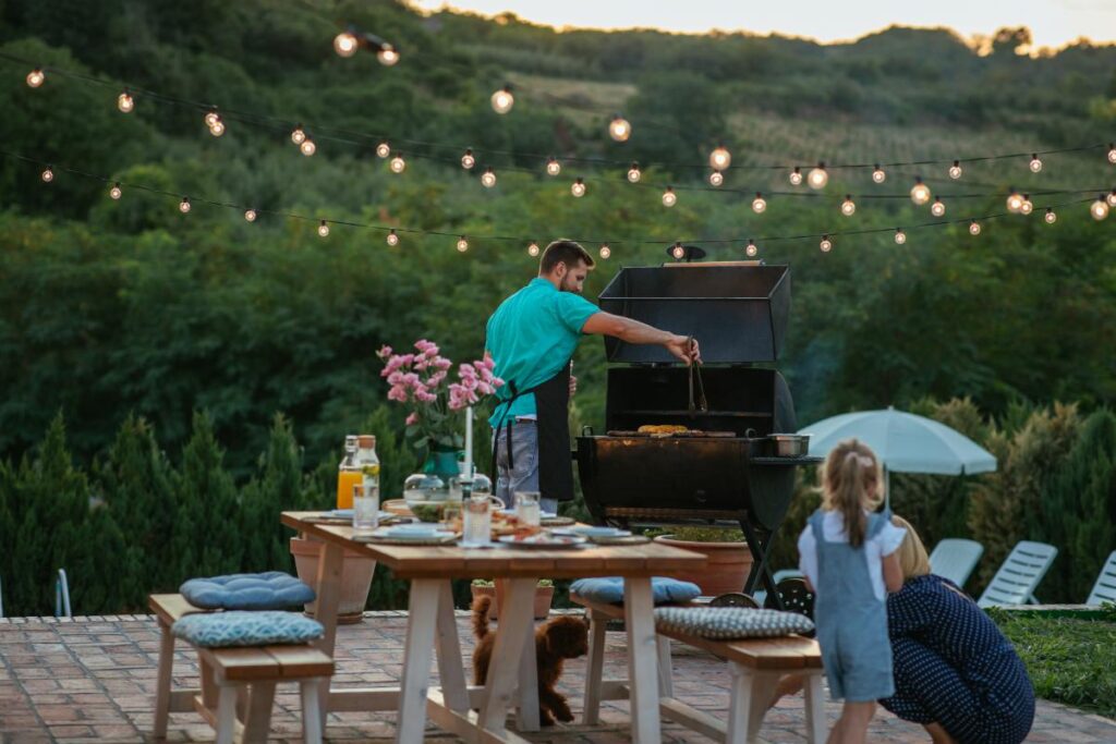 young-adult-man-barbecuing-while-his-wife-daughter-is-playing-with-dog